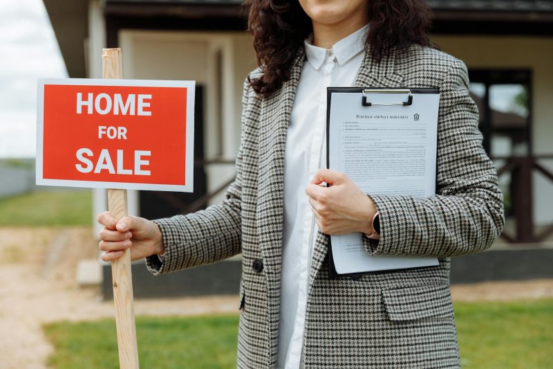 A real estate agent holding a home for sale sign and clipboa 1779814844